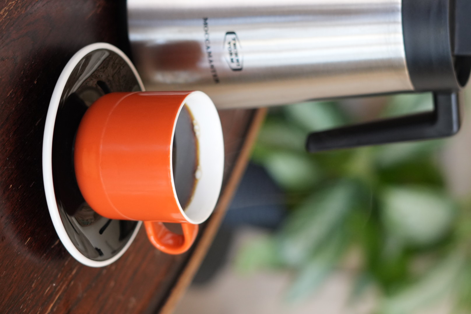 Orange cup of batch brew next to a Moccamaster