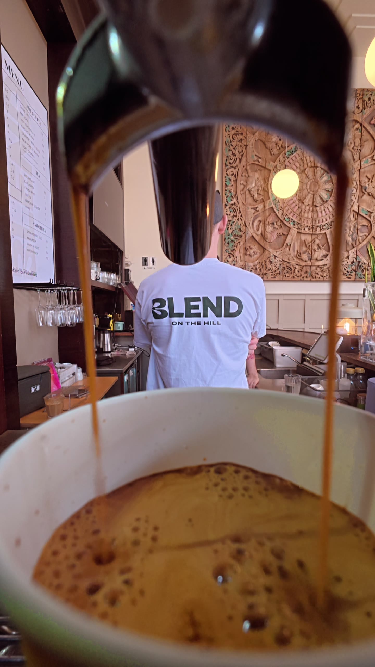 Double espresso pulling, barista in a Blend tee in the background