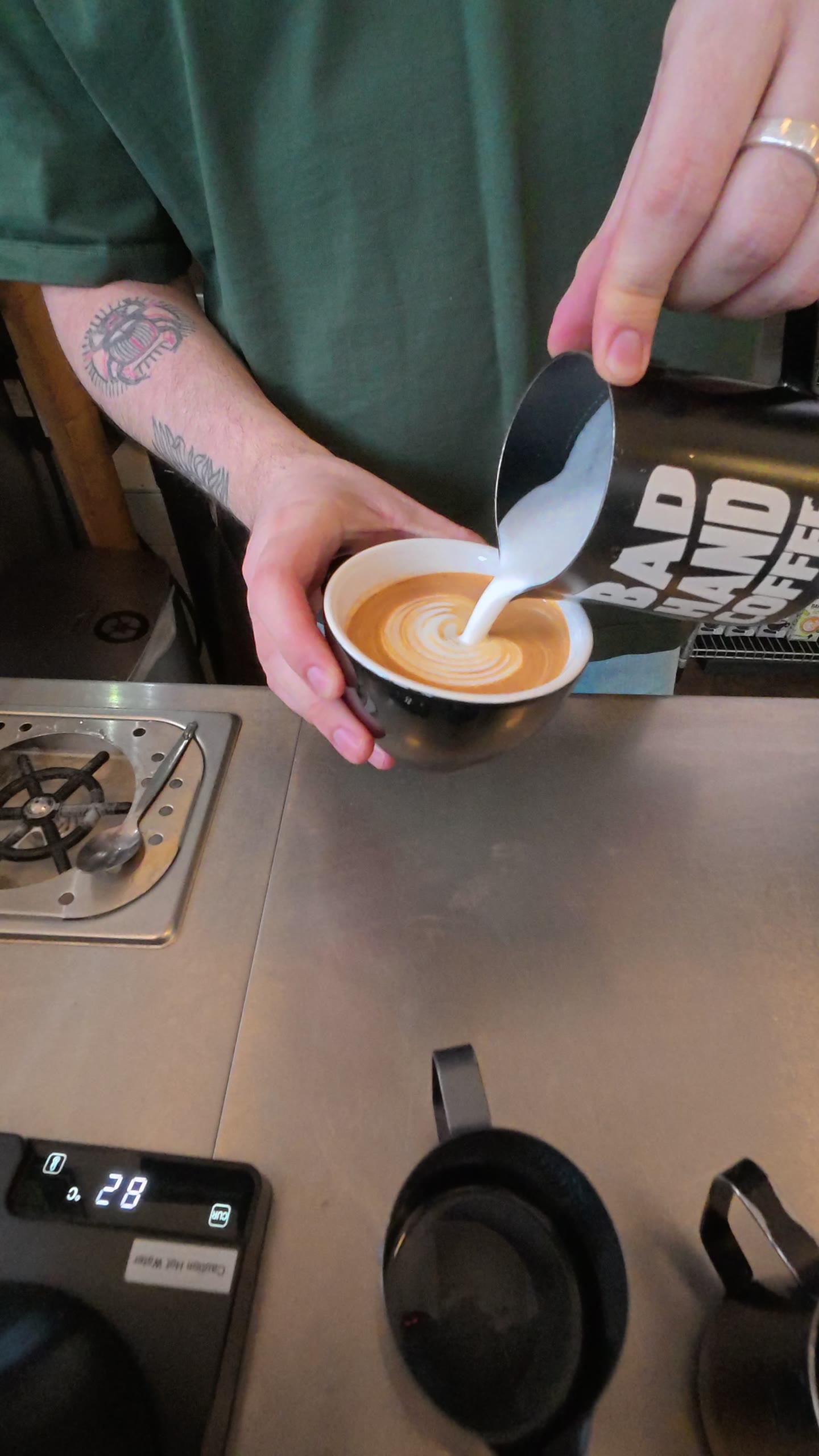 Barista pouring a rosetta into a black ceramic cup