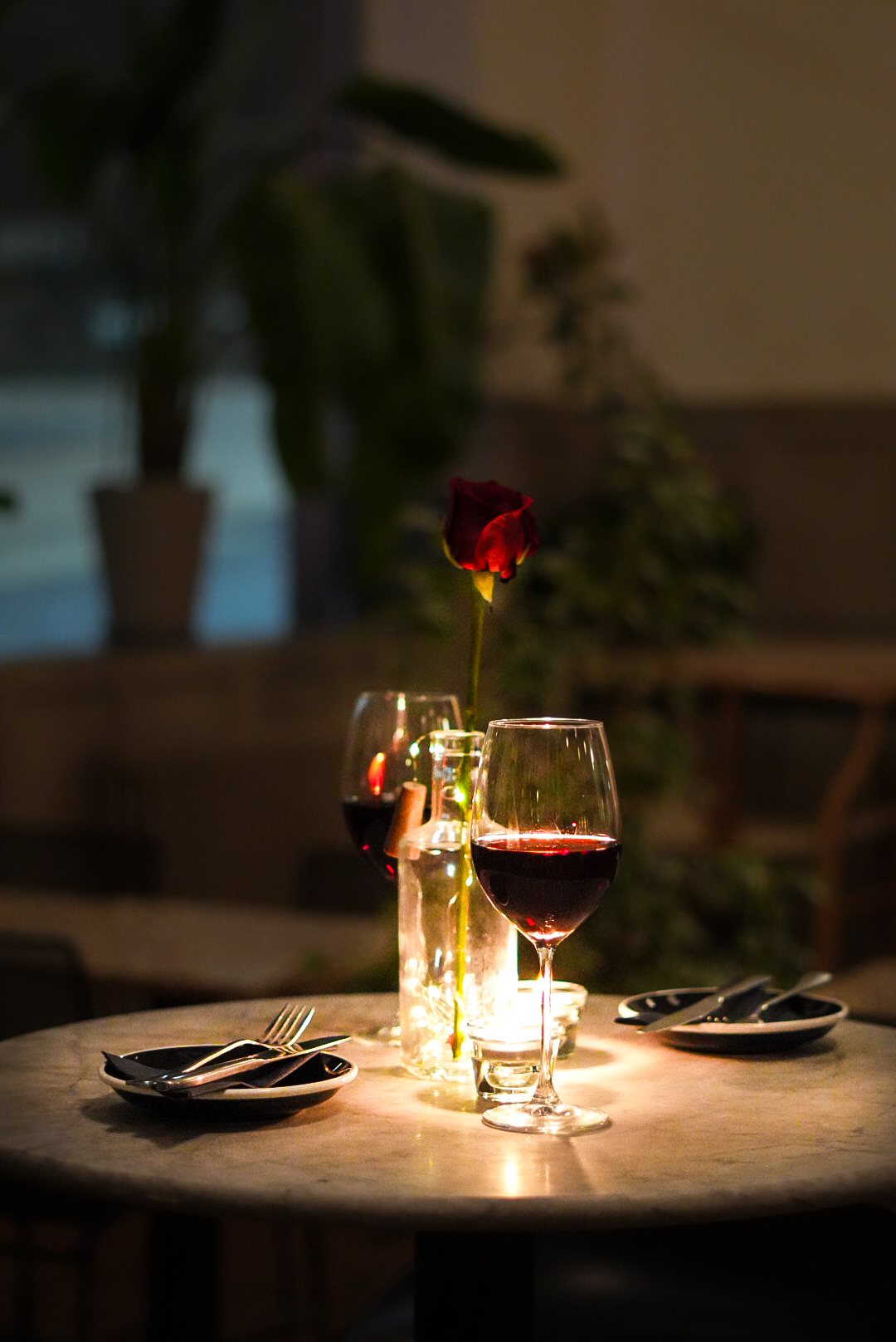 Candlelit table for two with red wine and a rose