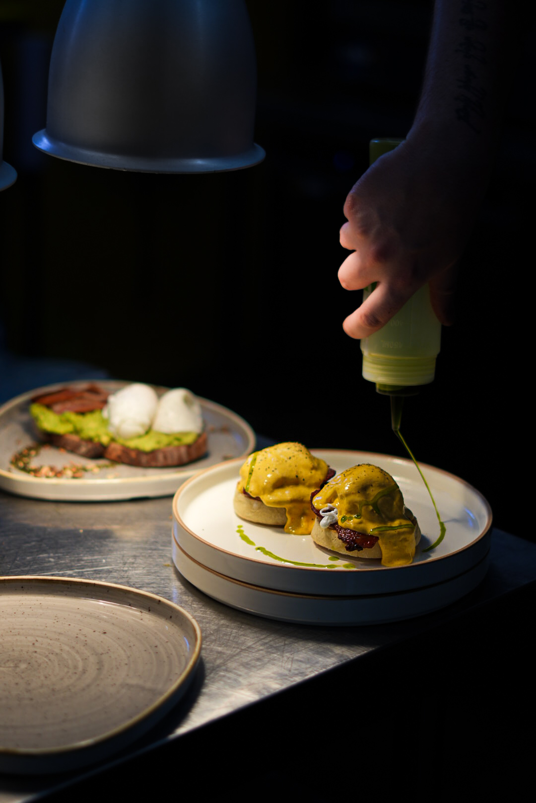 Eggs Benedict being finished with chive oil at the pass