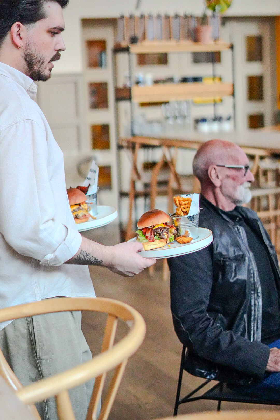 Server carrying two burgers with waffle fries through the room